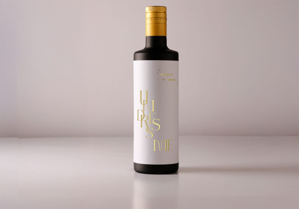 one bottle of vinegar without the label in the shape of a jacket, with as title undress me, printed in gold directly on a white undershirt